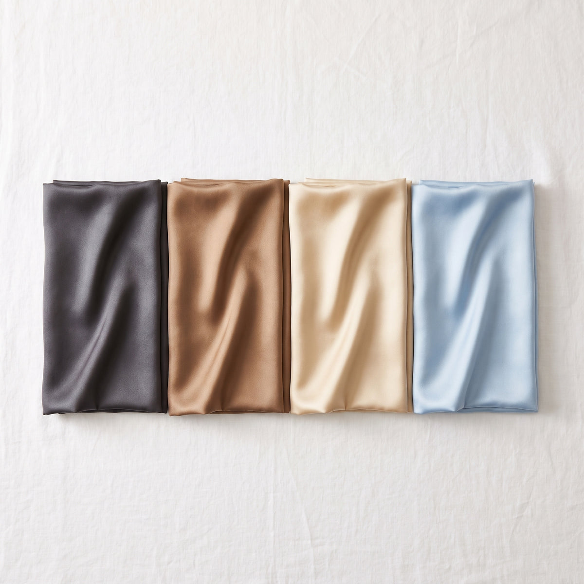 Alle vier Farben des Seidenkissenbezugs nebeneinander: Graphit, Karamell, Champagner, Himmelblau