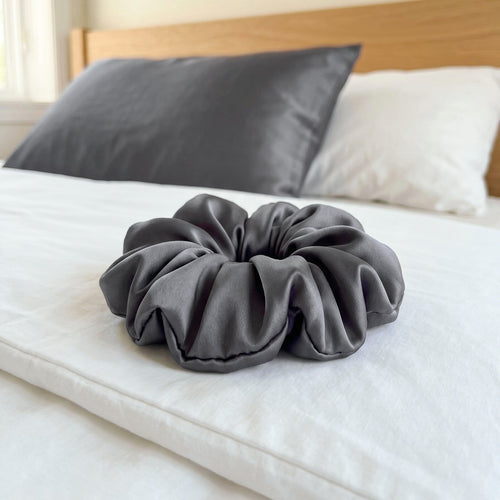 Seiden-Scrunchie in Graphit auf weißer Bettwäsche, dahinter der Seidenkissenbezug in Graphit