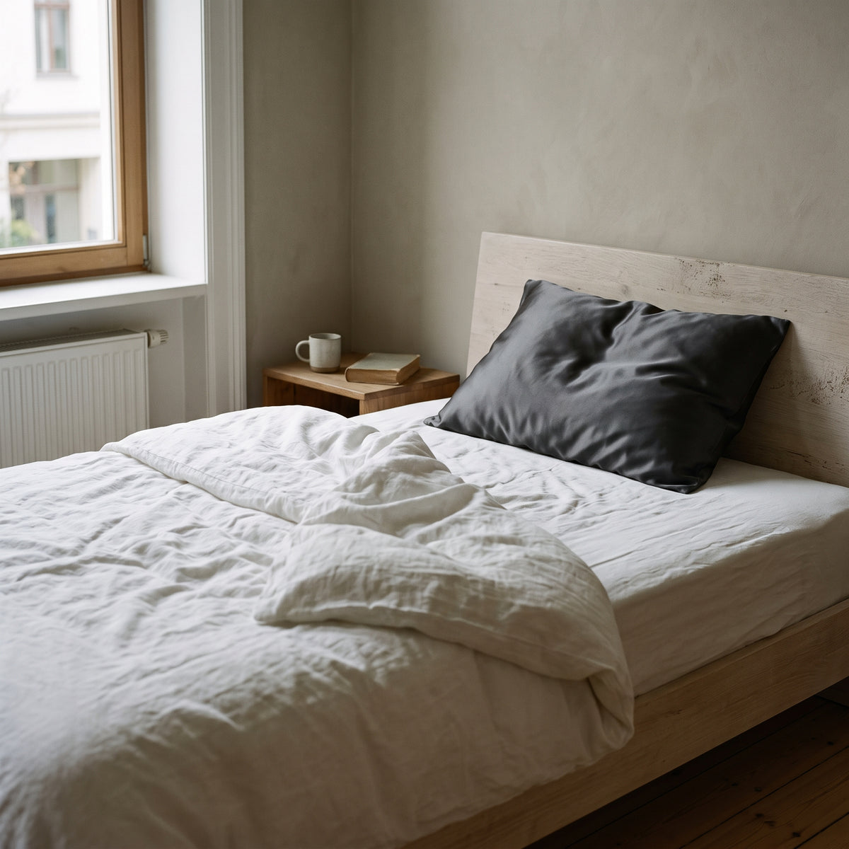Bett mit weißer Leinenbettwäsche und einem Seidenkissenbezug in Graphit im Morgenlicht